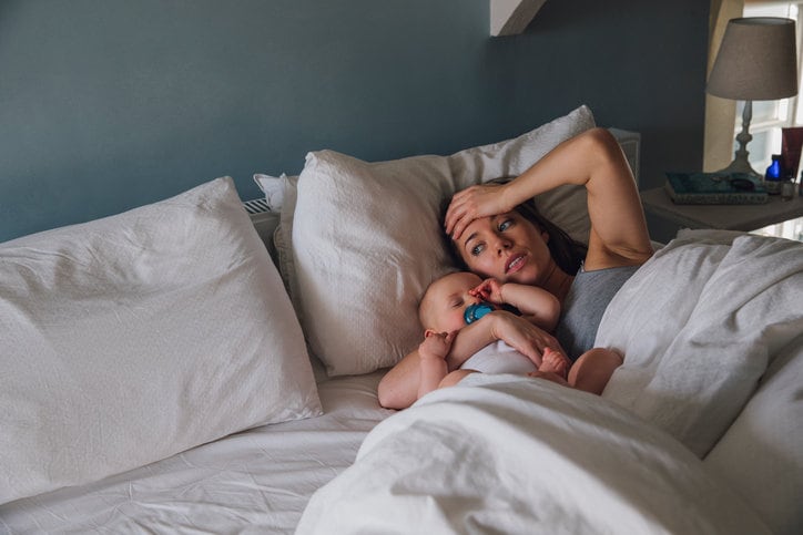 Fotografia di una mamma stanca nel letto accanto al neonato addormentato