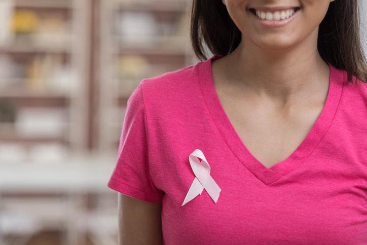Fotografia di una donna con una maglietta rosa e un fiocchetto appeso sul seno a testimonianza della vittoria contro il tumore.