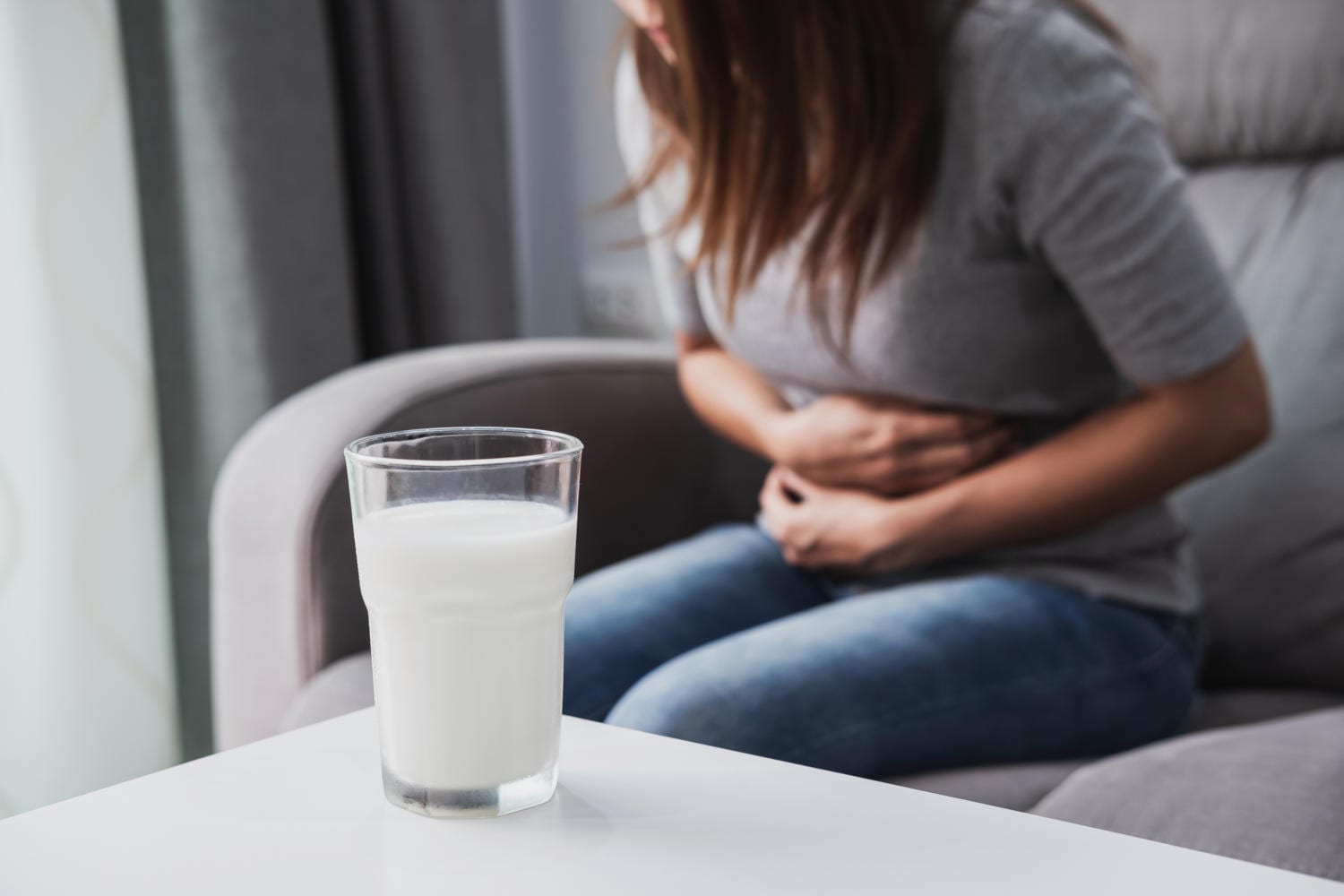 Donna che si tiene la pancia sullo sfondo e in primo piano un bicchiere di latte
