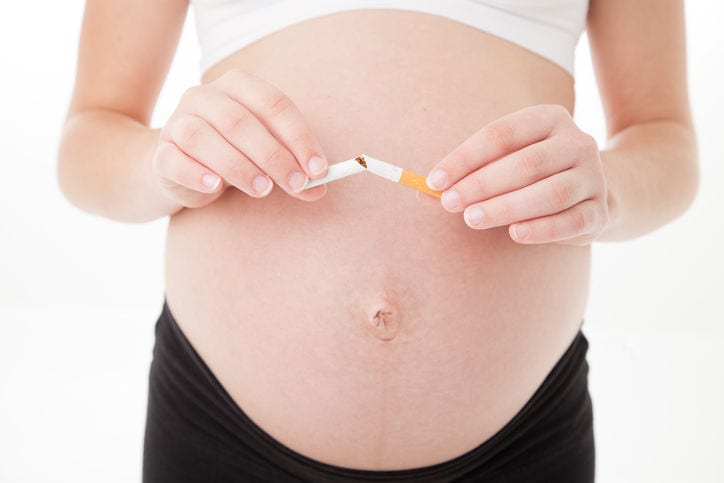 Primo piano di un pancione, di fronte al quale la mamma spezza a metà una sigaretta.
