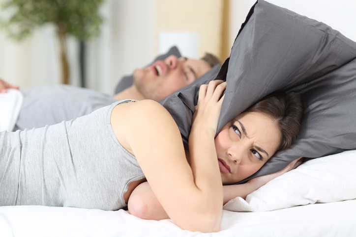 Donna che cerca di attutire il russamento del marito con il proprio cuscino.