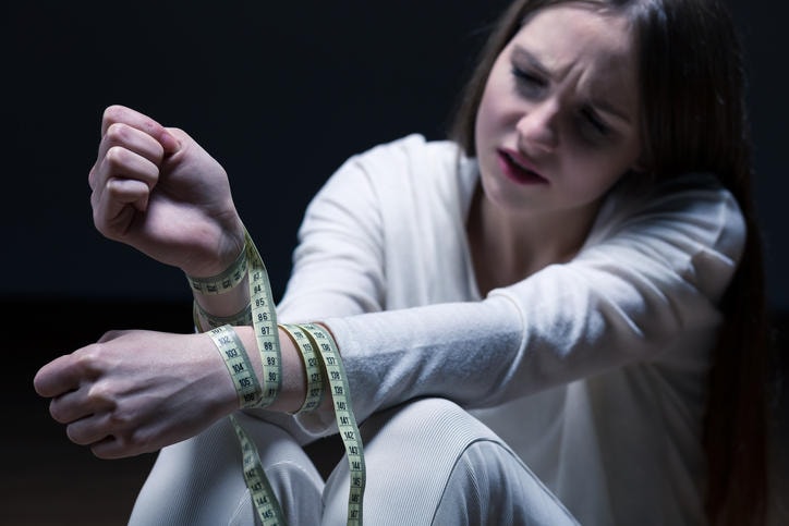 Fotografia di una ragazza con i polsi legati da un centimetro da sarta, per ricordare la prigione della bulimia.