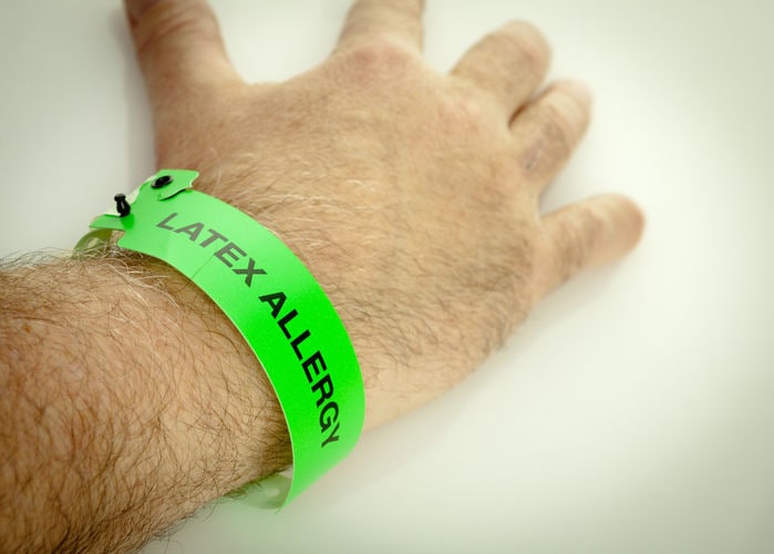 Fotografia di una mano con un braccialetto verde fluo e l'indicazione "Latex Allergy".