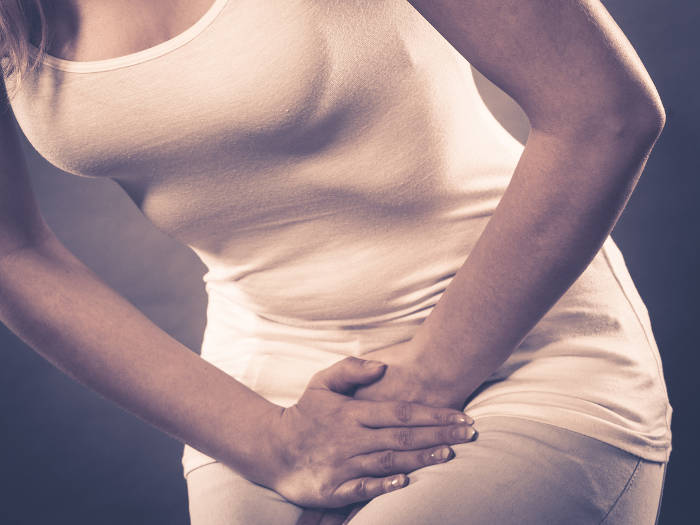 Fotografia di una donna che, a causa di dolore, appoggia le mani sulla regione pelvica