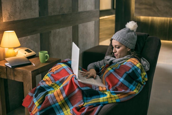 Fotografia di una donna in poltrona con coperta e cuffia perché sente freddo