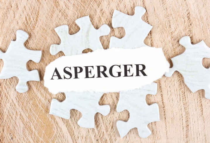 Scritta nera "Asperger" su fondo bianco, appoggiata su alcuni pezzi di un puzzle.