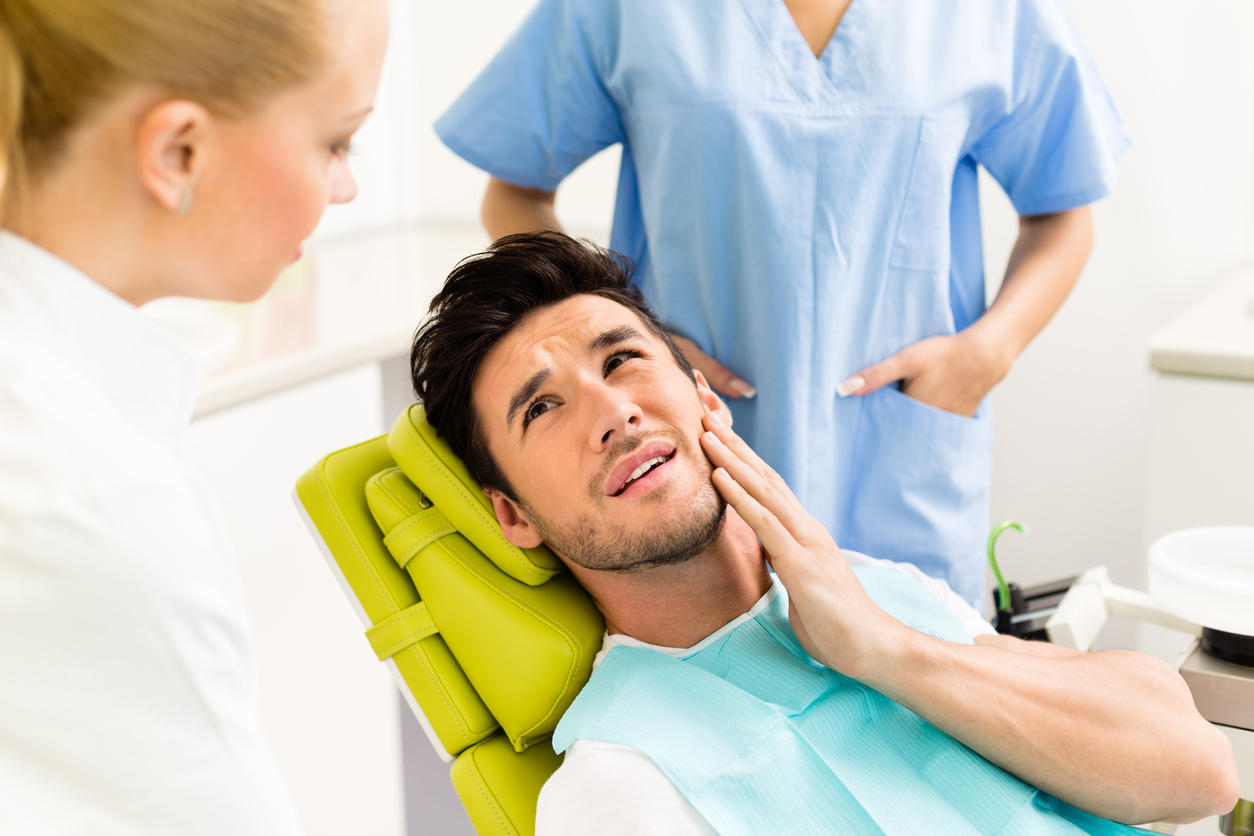 Paziente sul lettino del dentista che si tocca la guancia a causa del dolore