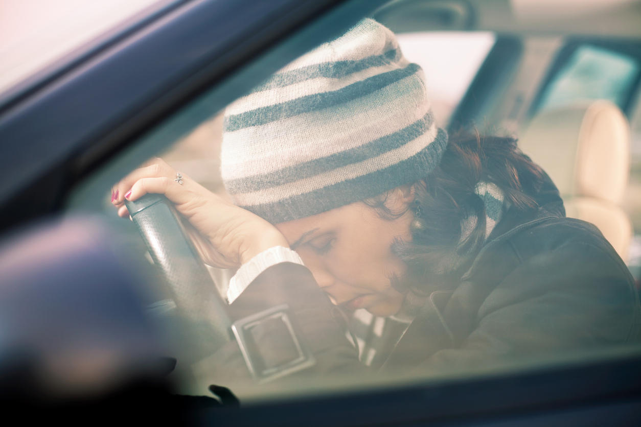 Donna in macchina con la testa appoggiata al volante e gli occhi chiusi