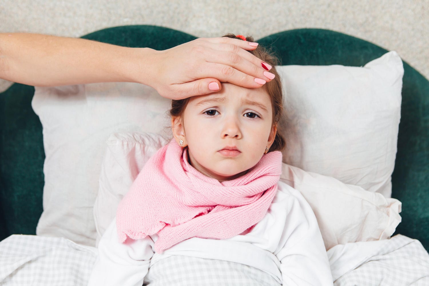 Bambina nel letto, con la mano di un genitore appoggiata alla fronte