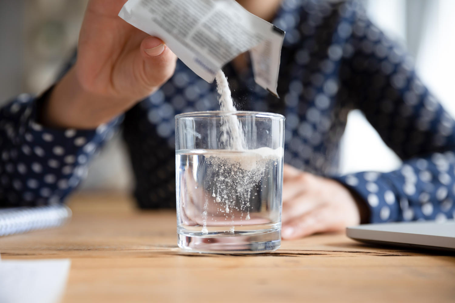 Donna versa bustina di farmaco in un bicchiere d'acqua