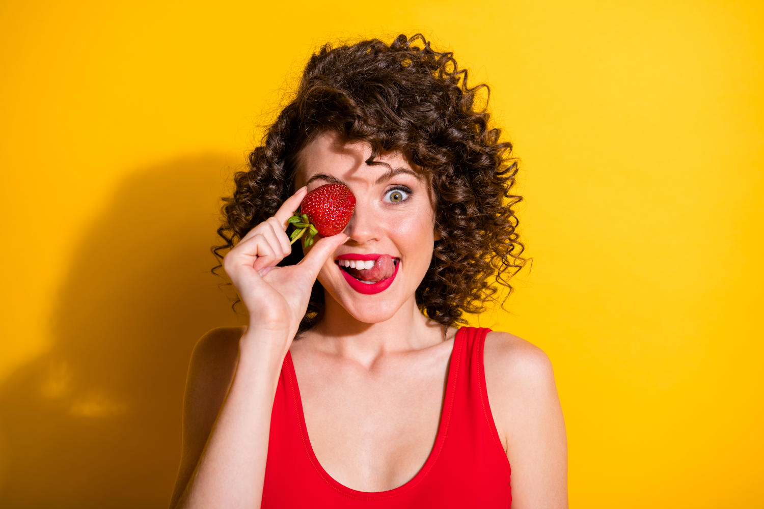 Ragazza che sorride con la lingua di fuori e una fragola sull'occhio