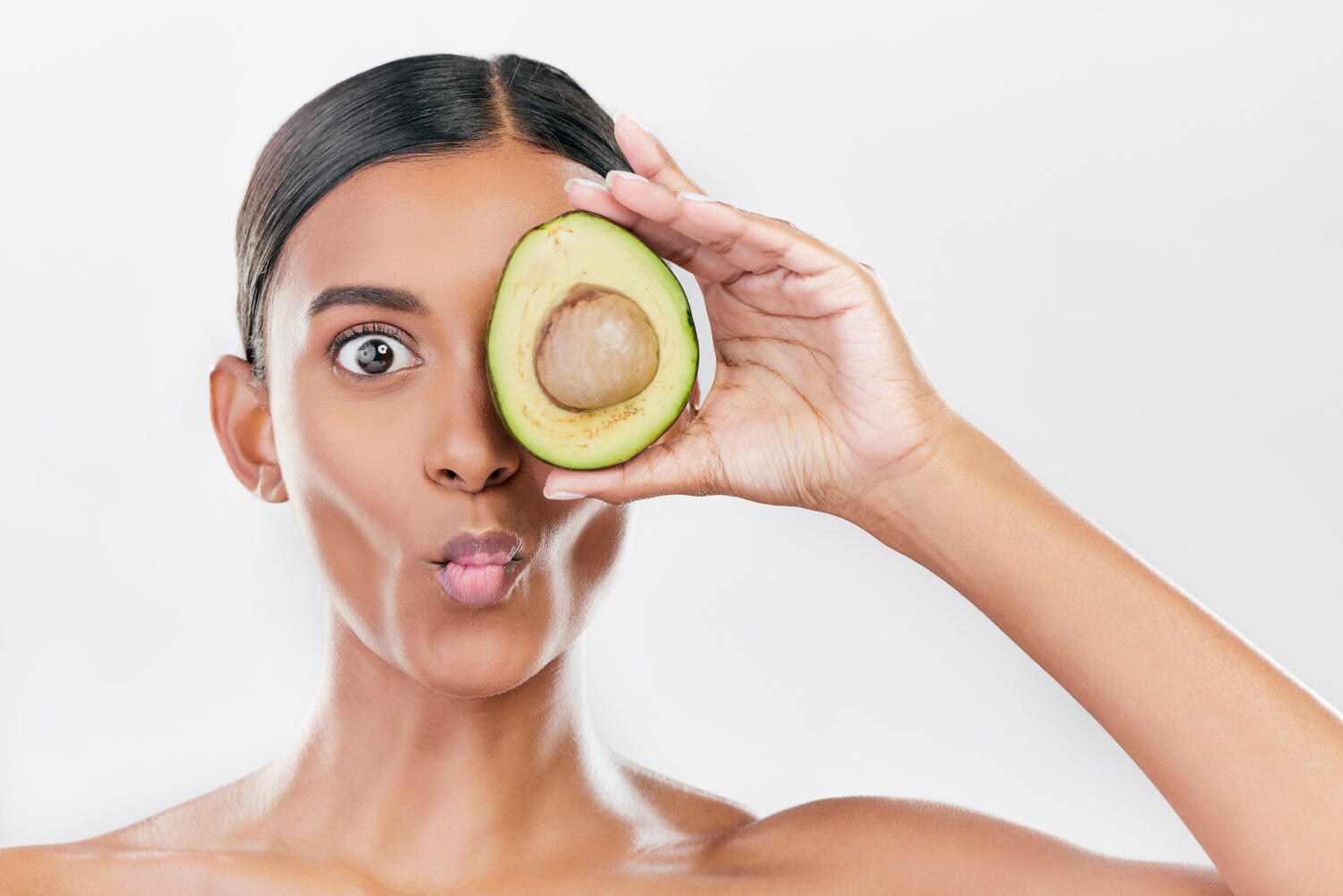 Ragazza che fa una faccia buffa e appoggia mezzo avocado sul'occhio