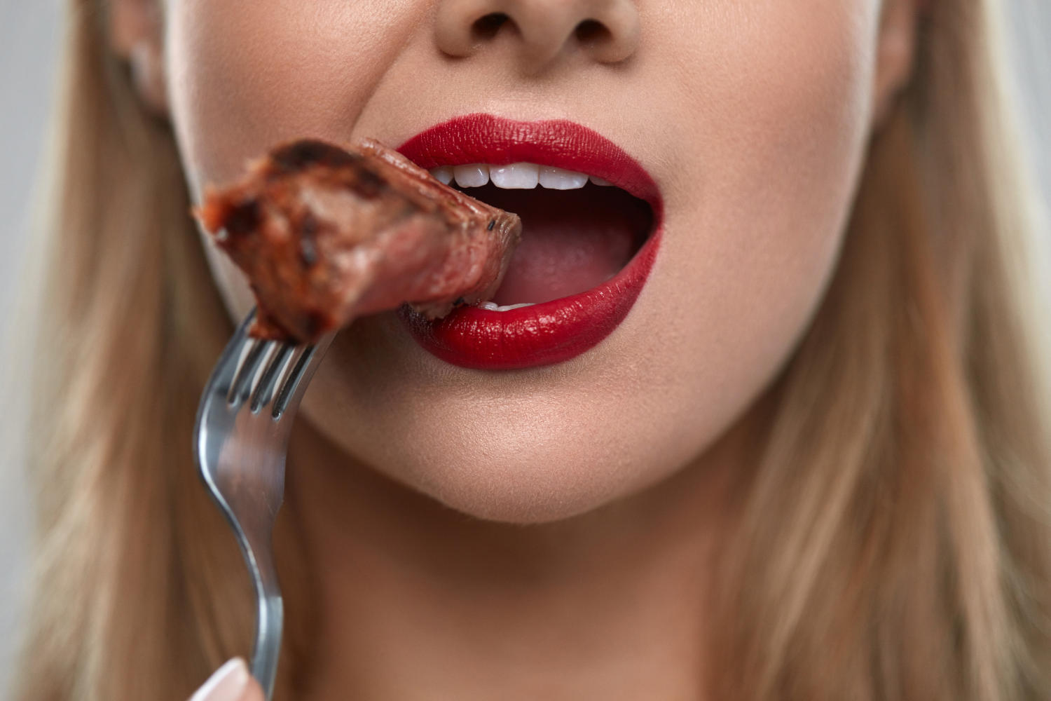 Primo piano della bocca di una donna che sta mangiare un boccone di carne