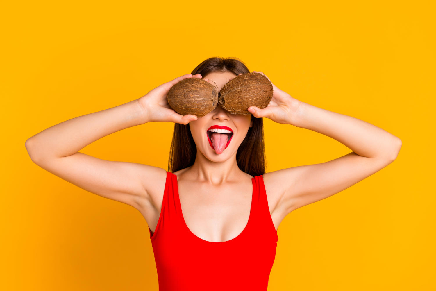 Ragazza tiene due noci di cocco davanti agli occhi e tira fuori la lingua