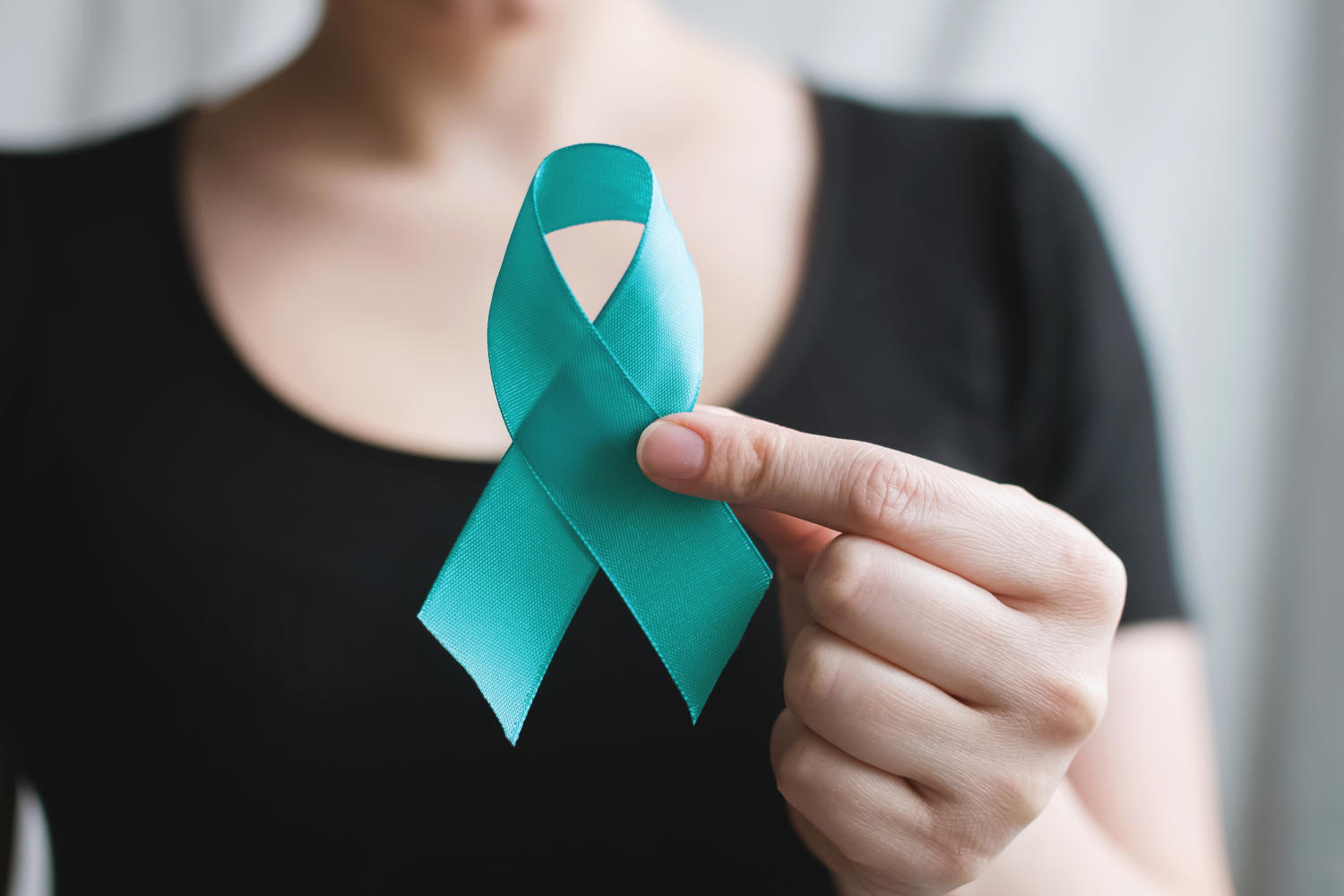 Donna che tiene in mano un nastro color verde acqua, simbolo del cancro cervicale, del cancro ovarico, del cancro ginecologico in genere