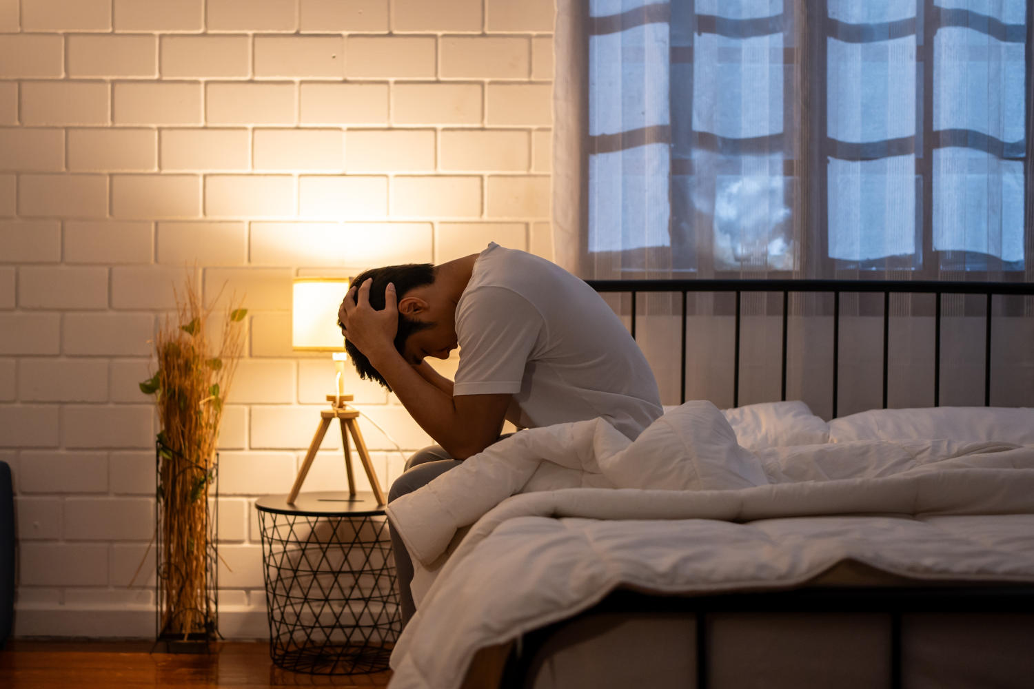 Uomo frustrato che non riesce a dormire, seduto sul letto