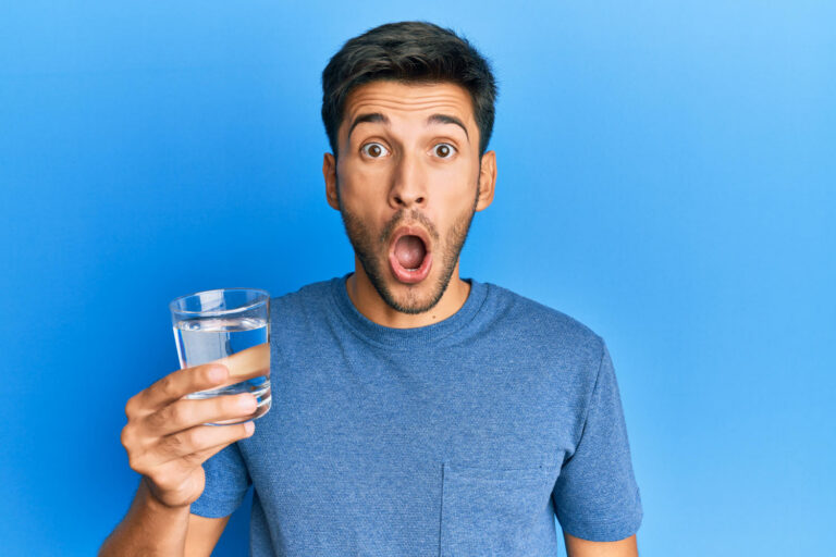 Uomo con bicchiere d'acqua in mano e sguardo stupito