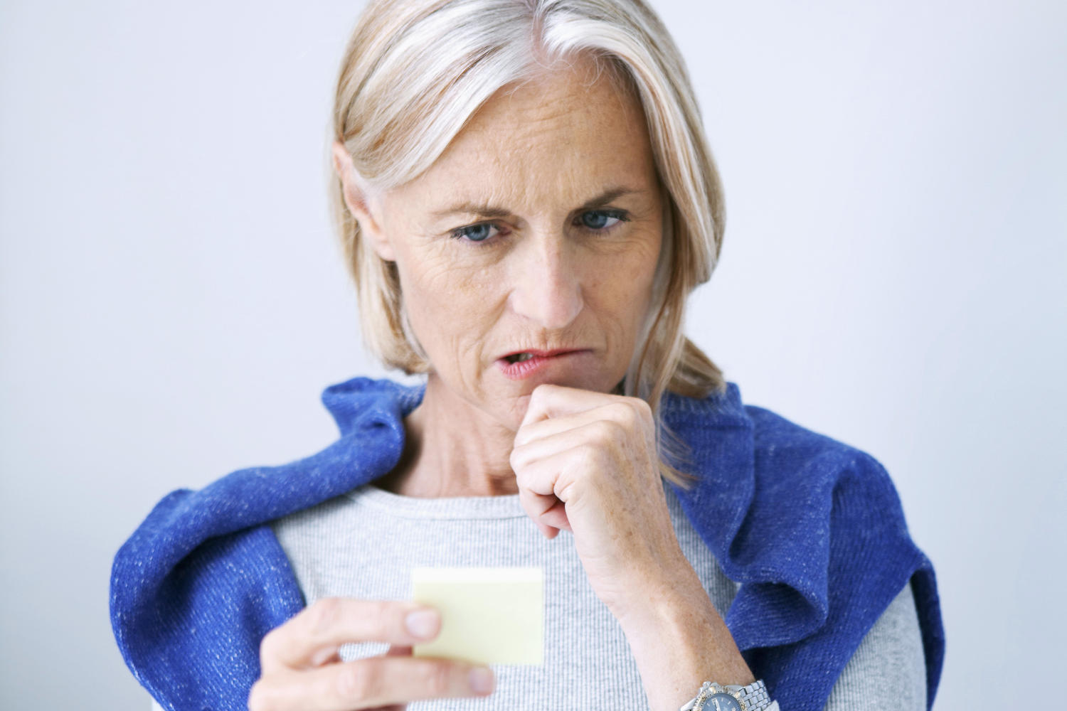 Donna di 50 anni che guarda un post-it con sguardo corrucciato