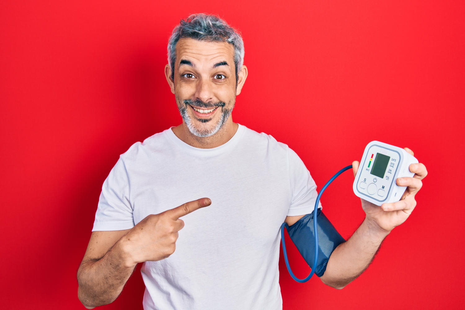 Uomo di mezza età con i capelli grigi che usa il misuratore di pressione sanguigna sorridendo felice e indicando con mano e dito