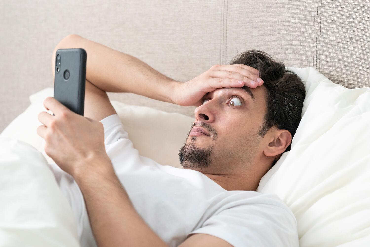 Uomo che controlla il cellulare dal letto con sguardo sorpreso
