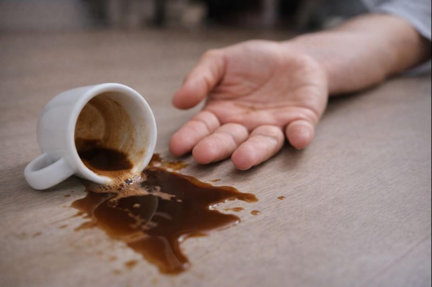 Tazzina di caffè rovesciata per terra accanto alla mano di una persona svenuta